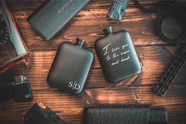 Black steel flasks engraved with initials on one and a script message on the other