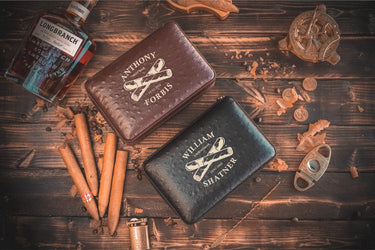Brown and black cigar travel cases, each engraved with a name and a crossed-cigars design