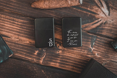 Two black flip-top lighters, one engraved with stacked initials, one with a handwritten note